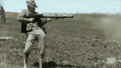 A Man In A Cowboy Hat Is Holding A Large Rifle In A Field GIF
