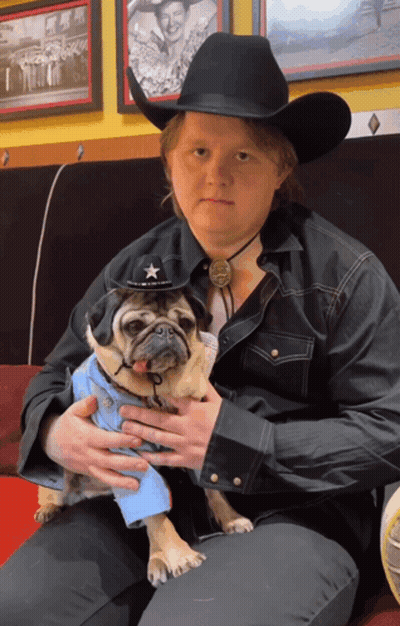 A Man In A Cowboy Hat Is Holding A Pug GIF
