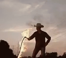 A Man In A Cowboy Hat Is Holding A Torch In Front Of A Flame . GIF
