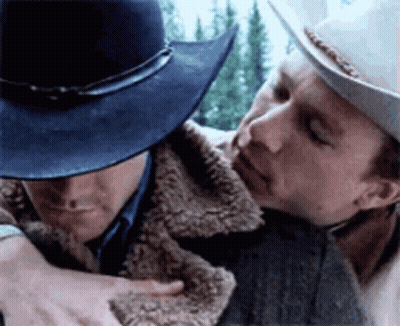 A Man In A Cowboy Hat Is Hugging Another Man In A Fur Coat GIF