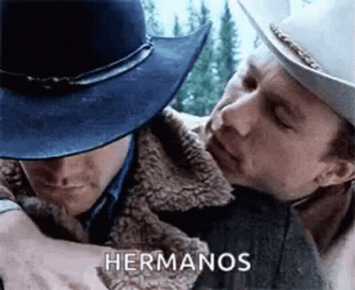 A Man In A Cowboy Hat Is Hugging Another Man In A Jacket . GIF