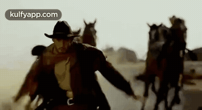 A Man In A Cowboy Hat Is Leading A Herd Of Horses Through A Desert . GIF