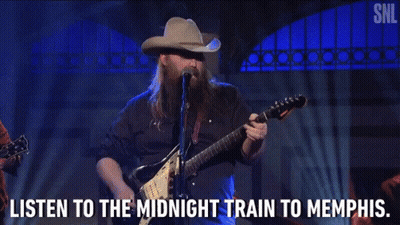 A Man In A Cowboy Hat Is Playing A Guitar And Singing Into A Microphone GIF