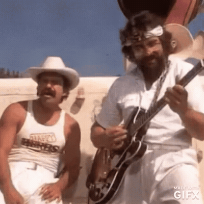 A Man In A Cowboy Hat Is Playing A Guitar Next To Another Man In White Pants . GIF