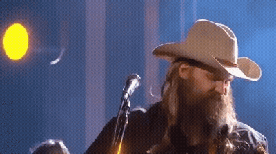 A Man In A Cowboy Hat Is Singing Into A Microphone . GIF