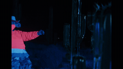 A Man In A Cowboy Hat Is Standing In Front Of A Cactus In The Dark GIF