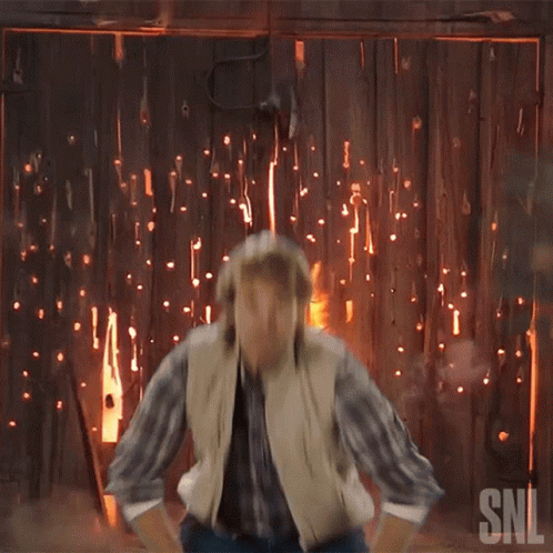 A Man In A Cowboy Hat Is Standing In Front Of A Fire With The Snl Logo On The Bottom GIF