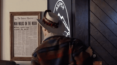 A Man In A Cowboy Hat Is Standing In Front Of A Framed Newspaper That Says Man Walks On The Moon GIF