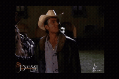 A Man In A Cowboy Hat Is Standing In Front Of A Sign That Says " Buena " GIF