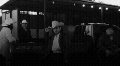 A Man In A Cowboy Hat Is Standing In The Back Of A Truck With The Number 454 On It GIF