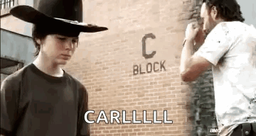 A Man In A Cowboy Hat Is Standing Next To A Man In A White Shirt In Front Of A Brick Wall . GIF