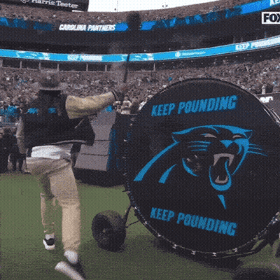 A Man In A Cowboy Hat Is Throwing A Baseball In A Stadium With A Banner For Harris Teeter GIF