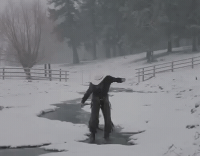 A Man In A Cowboy Hat Is Walking Across A Snow Covered Stream . GIF