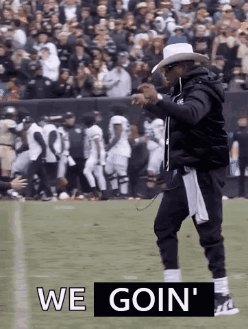 A Man In A Cowboy Hat Is Walking On A Football Field With The Words `` We Goin '' Written Above Him . GIF