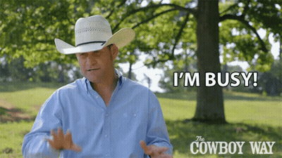 A Man In A Cowboy Hat Says " I 'M Busy " In Front Of A Tree GIF