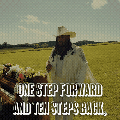 A Man In A Cowboy Hat Stands In A Field Next To A Piano With The Words One Step Forward And Ten Steps Back GIF