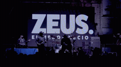 A Man In A Cowboy Hat Stands In Front Of A Zeus Sign GIF