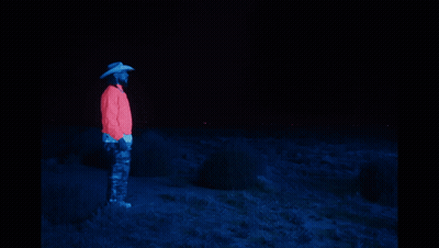 A Man In A Cowboy Hat Stands Next To A Glowing Horse In The Dark GIF