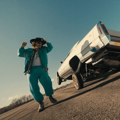 A Man In A Cowboy Hat Stands Next To A White Car On Its Rear Wheels GIF