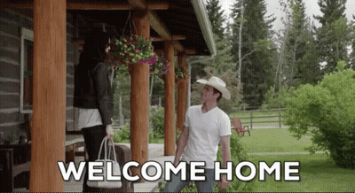 A Man In A Cowboy Hat Stands On A Porch With A Woman Holding A Bag And The Words Welcome Home Above Him GIF