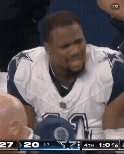 A Man In A Cowboys Uniform Is Sitting In The Stands During A Football Game . GIF