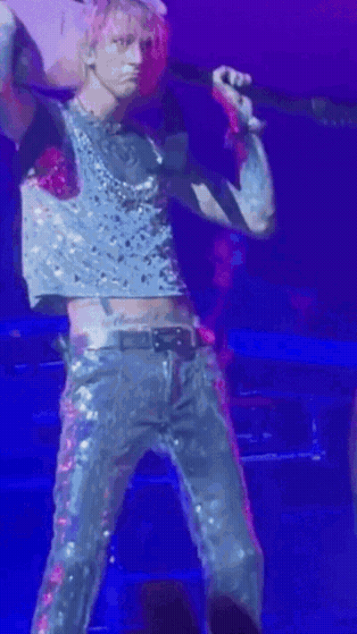 A Man In A Crop Top Is Holding A Guitar And Singing Into A Microphone . GIF