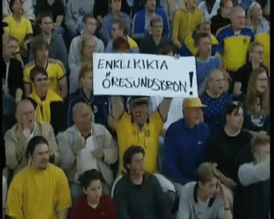 A Man In A Crowd Holds Up A Sign That Says " Enklrikta " On It GIF