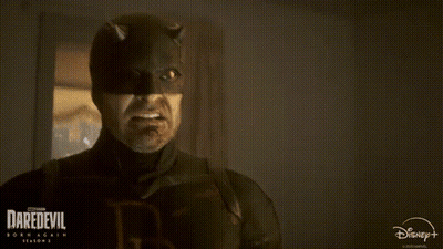 A Man In A Daredevil Costume Is Smiling In A Dark Room . GIF