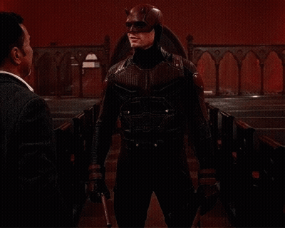 A Man In A Daredevil Costume Is Talking To Another Man In A Church GIF