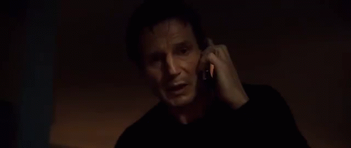 A Man In A Dark Room Is Talking On A Cell Phone . GIF