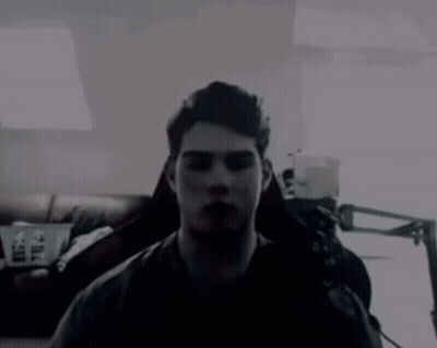 A Man In A Dark Room With A Couch And A Lamp In The Background GIF