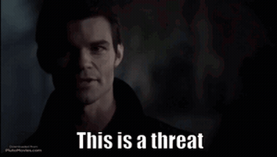 A Man In A Dark Room With The Words This Is A Threat Below Him GIF