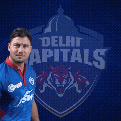 A Man In A Delhi Capitals Jersey Stands In Front Of The Team Logo GIF