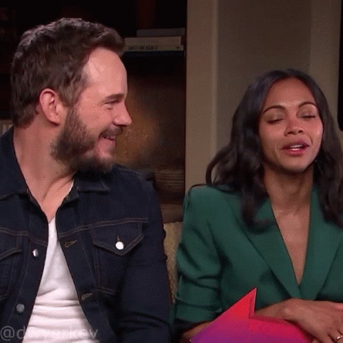 A Man In A Denim Jacket And A Woman In A Green Jacket Sit On A Couch With Their Eyes Closed GIF
