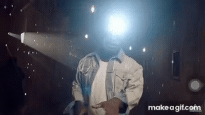 A Man In A Denim Jacket Is Dancing In Front Of A Projector Screen . GIF