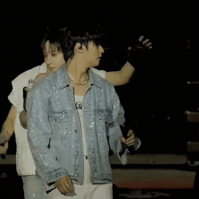 A Man In A Denim Jacket Is Holding A Microphone On A Stage GIF