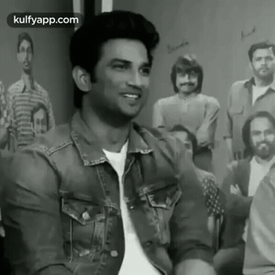 A Man In A Denim Jacket Is Sitting In Front Of A Group Of People . GIF