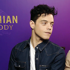 A Man In A Denim Jacket Is Sitting In Front Of A Purple Wall With The Word Ody In Gold Letters GIF