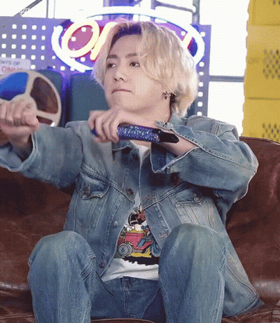 A Man In A Denim Jacket Is Sitting On A Couch Holding A Remote Control GIF