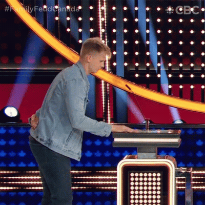 A Man In A Denim Jacket Is Standing In Front Of A Podium With The Words Family Feud Canada Written On It GIF