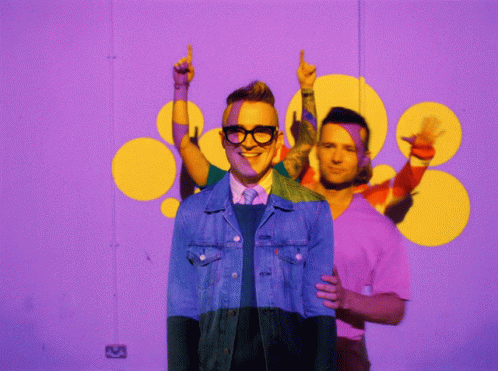 A Man In A Denim Jacket Is Standing In Front Of A Purple Background GIF