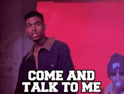 A Man In A Denim Jacket Is Standing In Front Of A Red Wall And Talking To Another Man . GIF