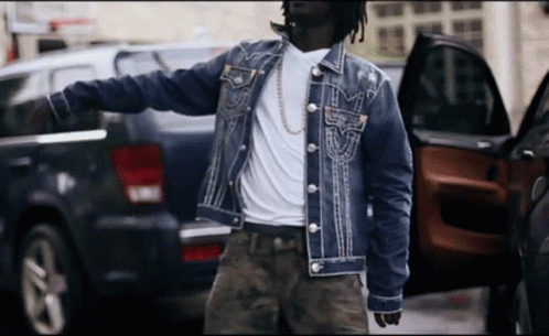 A Man In A Denim Jacket Is Standing Next To A Black Suv GIF