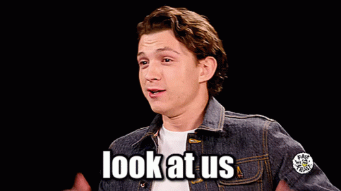 A Man In A Denim Jacket Says Look At Us With His Hands In The Air GIF