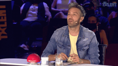 A Man In A Denim Jacket Sits At A Table With A Microphone In Front Of The Word Talent GIF