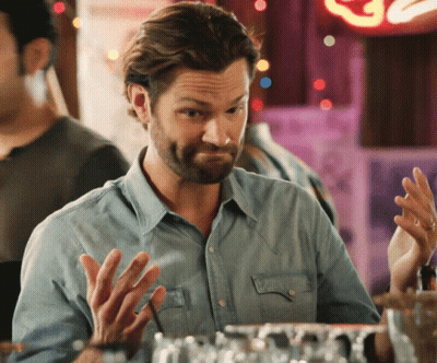 A Man In A Denim Shirt Is Sitting At A Bar With His Hands Up GIF