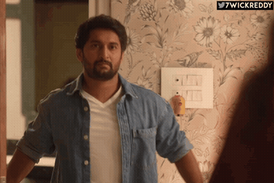 A Man In A Denim Shirt Is Standing In Front Of A Wall With Flowers On It And The Words 7Wickreddy Below Him GIF