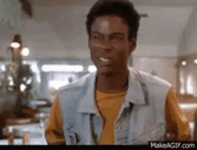 A Man In A Denim Vest And Yellow Shirt Is Standing In A Kitchen . GIF