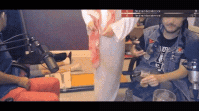 A Man In A Denim Vest Is Sitting In Front Of A Microphone While A Woman Stands In Front Of Him GIF