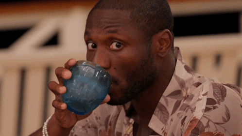 A Man In A Floral Shirt Drinks From A Blue Cup GIF